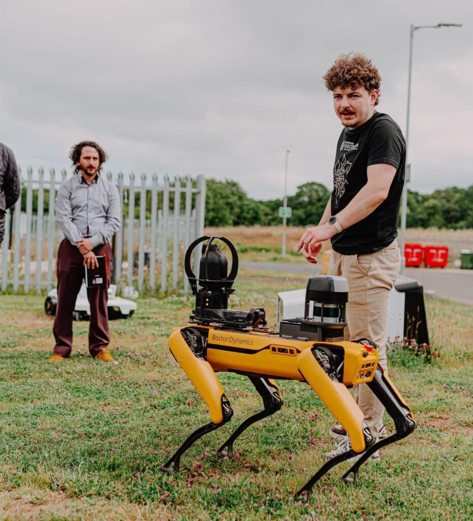 Man explaining Spot the robot to a group of people standing in a field